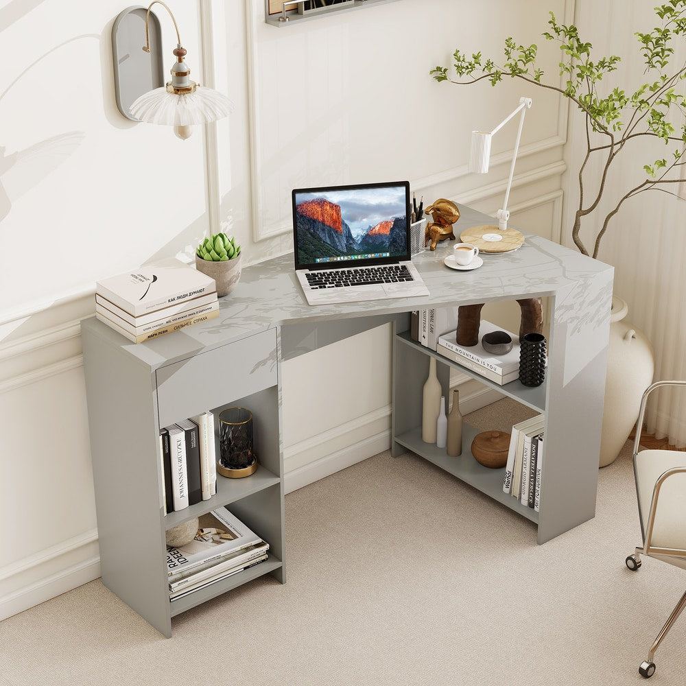 Grey L-shaped computer desk with open shelves and a drawer in a room