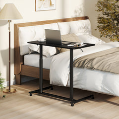 The office desk placed beside a bed with a laptop and reading material on the black tabletop