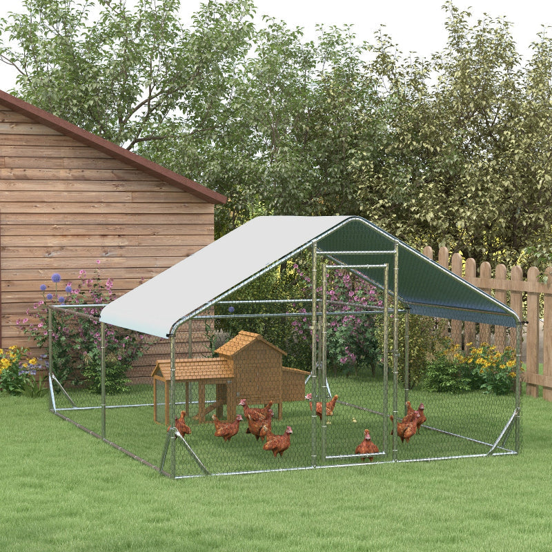 Outdoor chicken coop with a green roof and wire walls, surrounded by grass and trees.
