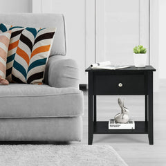 The black nightstand with a drawer and shelf positioned next to a sofa