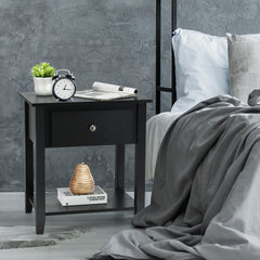The black side table used as a bedside unit with an alarm clock and books on the surface
