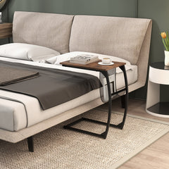 Compact sofa side snack table next to a bed with a book and cup on top