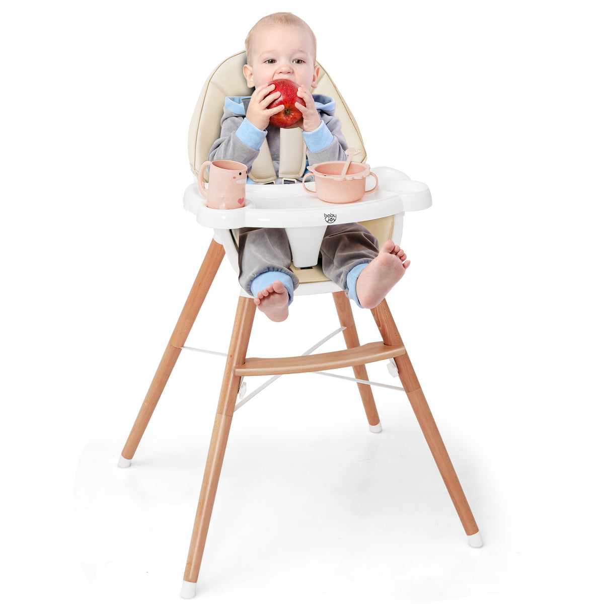 The high chair with a baby sitting in it eating an apple and holding a small cup