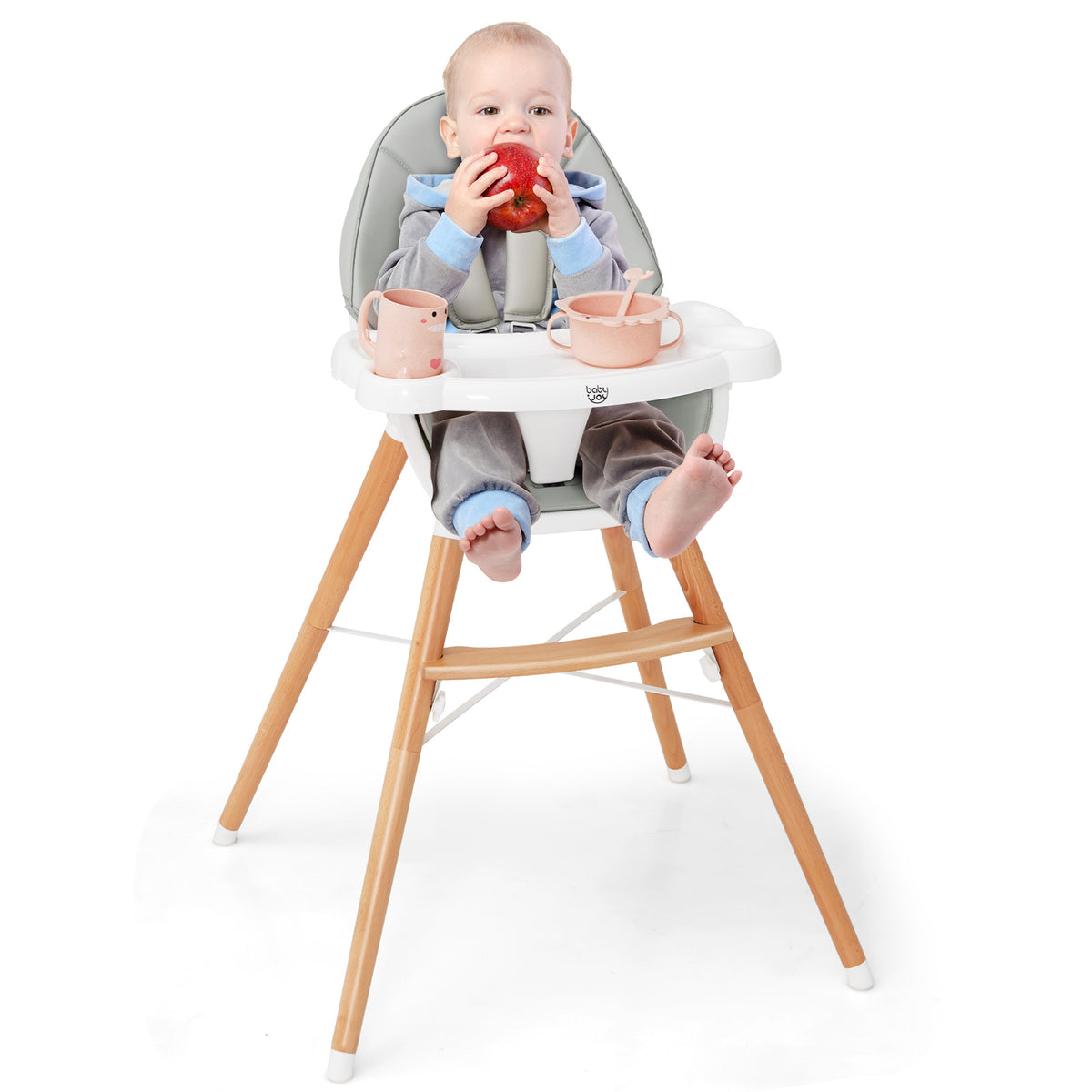 A baby sitting in the wooden baby infant high chair eating an apple