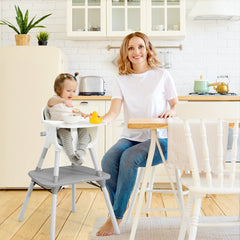 A woman feeding a baby in the grey high chair in a kitchen setting