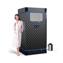 A woman in a white robe stands next to the black portable steam sauna, with the steam generator unit beside it