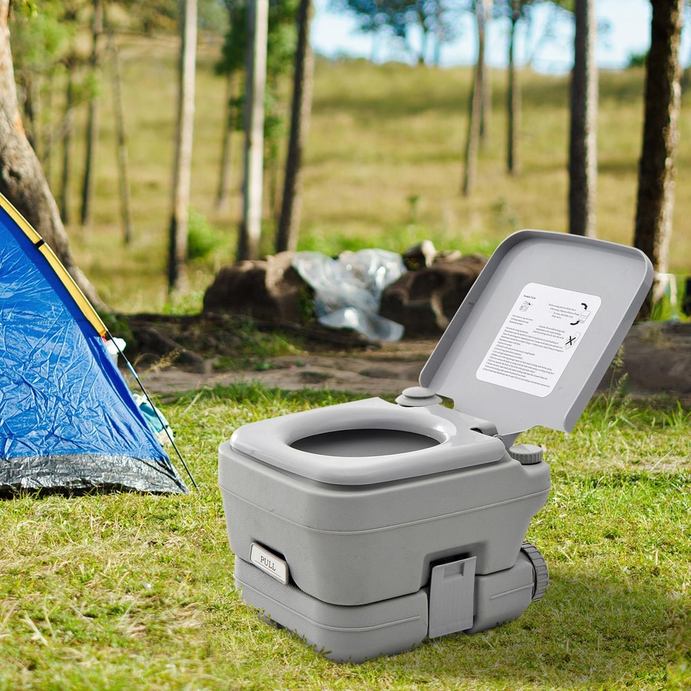 The camping toilet placed on grass next to a blue tent in a sunny outdoor woodland setting