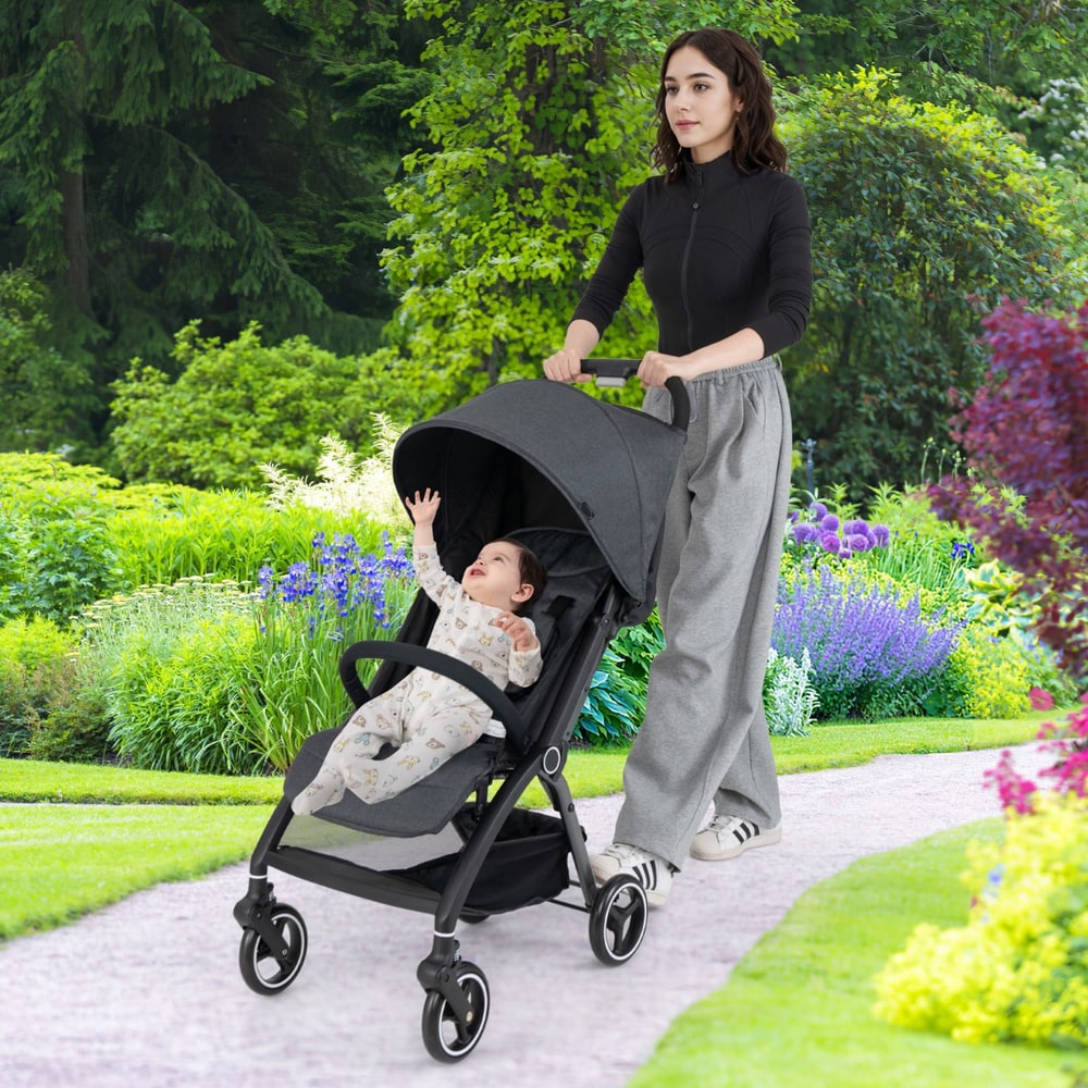 Woman pushing the grey baby stroller with a baby inside, on a paved path in a park