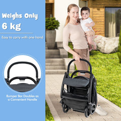 Woman holding a baby next to the grey baby stroller, which is folded
