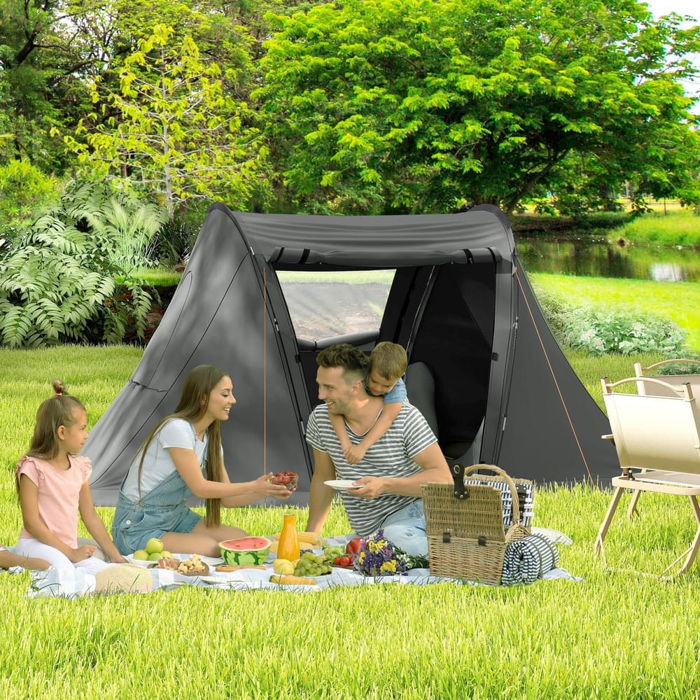 A family enjoying a picnic outside a grey three man camping tent pitched on grass in a park