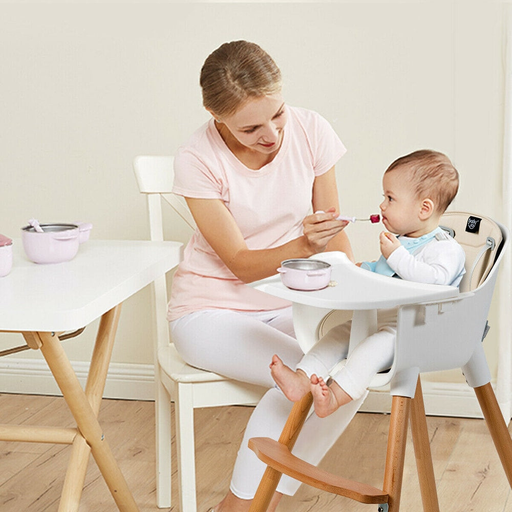 The wooden high chair with a white tray and beige padded seat