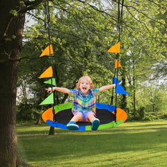 A happy child sitting on the round saucer swing set hanging from a tree in a green park